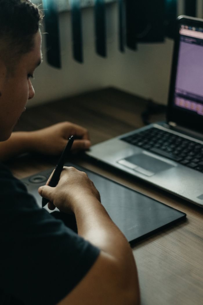 Home Person using digital tablet with stylus in a creative setup featuring a laptop indoors.