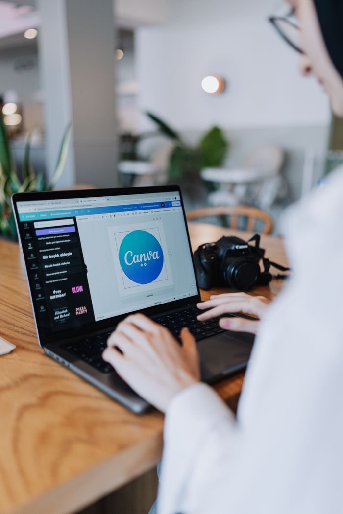 Home Young woman designing with Canva on laptop in a stylish indoor setting, accompanied by a digital camera.